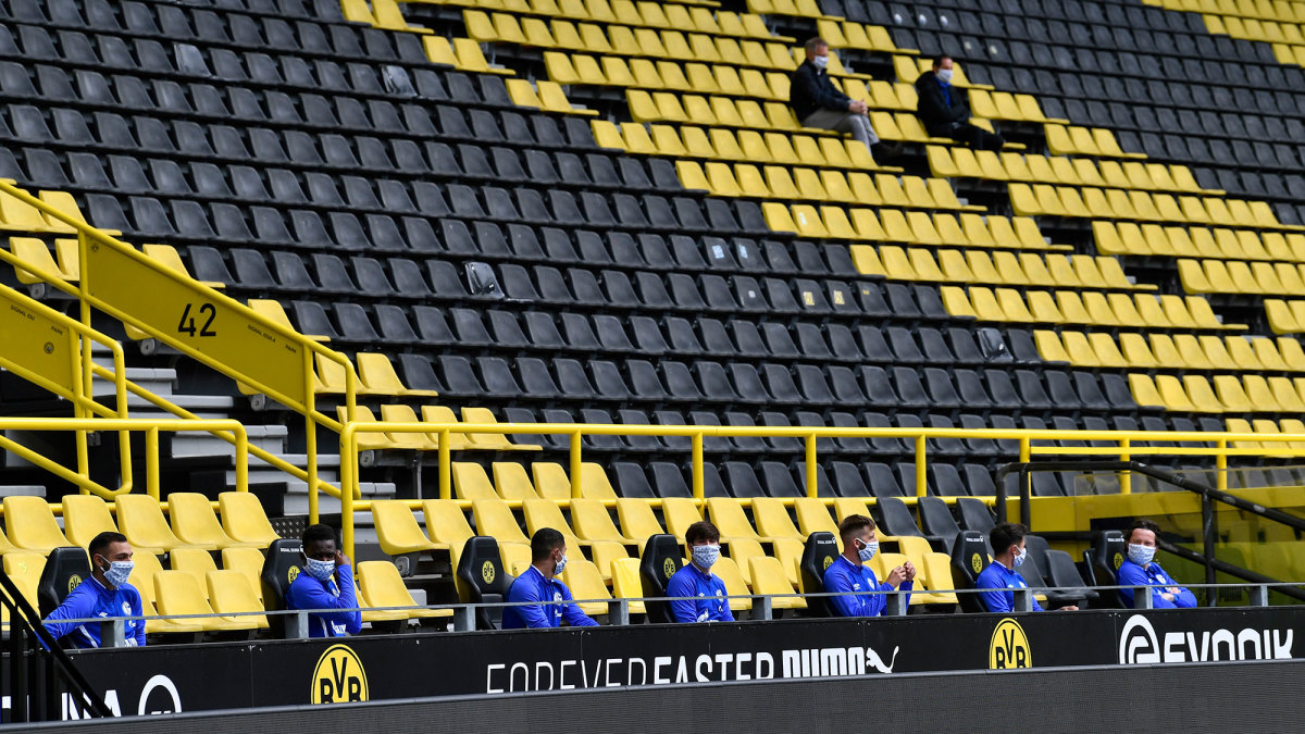 Schalke substitutes sit spread apart in the Dortmund stands